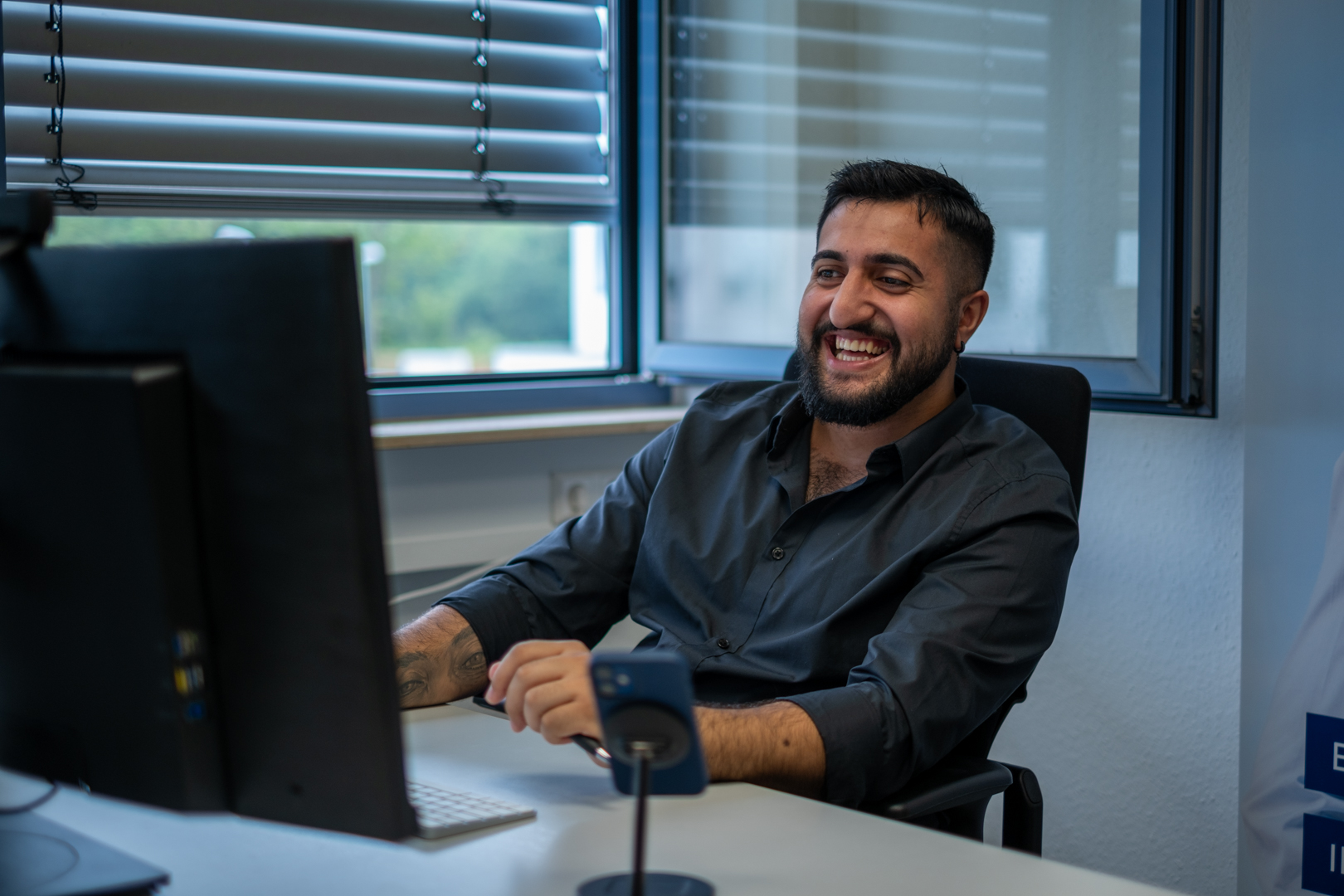 Ein Mann sitzt lachend vor einem Bildschirm am Schreibtisch